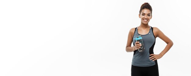 Healthy and Fitness concept beautiful African American girl in sport clothes holding water bottle after workout Isolated on white studio background