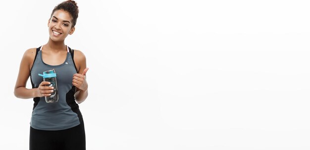 Здоровая и фитнес-концепция красивая афроамериканка в спортивной одежде, держащая бутылку с водой после тренировки Изолированная на белом фоне студии