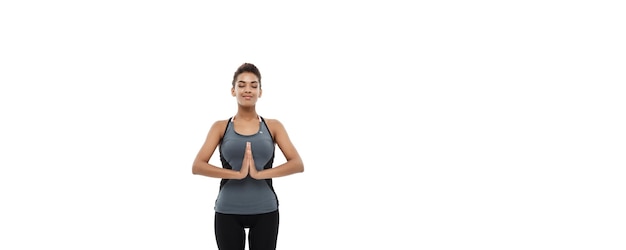 Concetto di salute e fitness bella signora africana americana in abbigliamento fitness facendo yoga e meditazione isolata su sfondo bianco