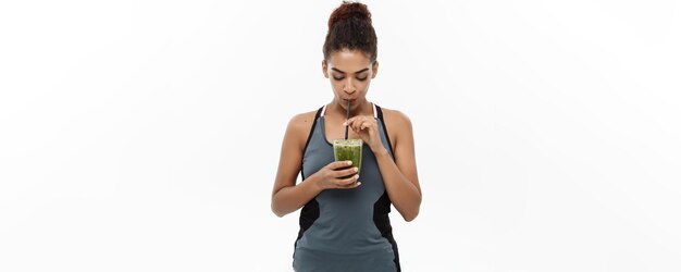 Healthy and Fitness concept Beautiful American African lady in fitness clothing drinking healthy vegetable drink Isolated on white background