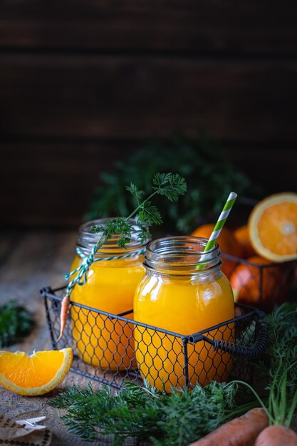 健康食品。暗い木製の背景に金属製のバスケットのガラスの瓶にオレンジとニンジンとニンジンジュース。コピースペース