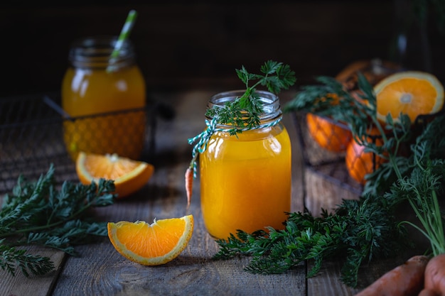 Foto gratuita cibo sano carote e succo di carota con arancia in un vaso di vetro in un cestino di metallo su uno sfondo di legno scuro spazio per la copia