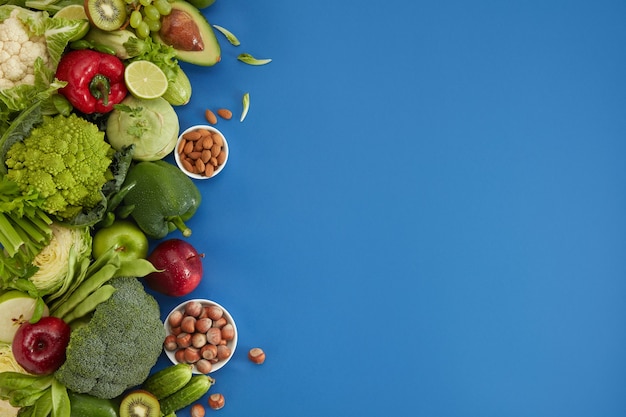 Healthy food dish on blue background. Healthful set including vegetables and fruits. Grape, apple, kiwi, pepper, lime, cabbage, zucchini, grapefruit, nuts. Proper nutrition or vegetarian menu.