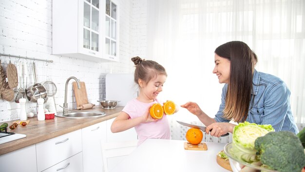 自宅で健康食品。台所で幸せな家族。母と子の娘が野菜や果物を準備しています。ビーガンフード