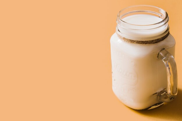 Healthy fresh milk in the glass jar with handle over the orange backdrop