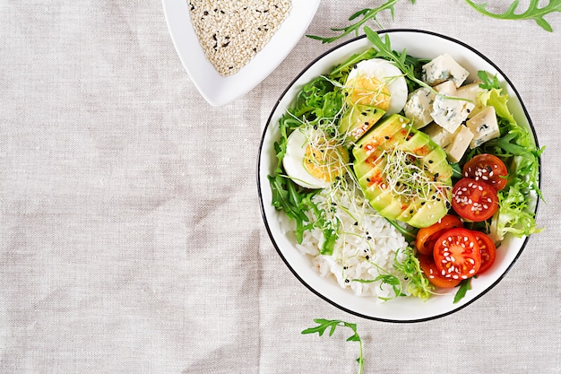 免费照片健康绿色素食佛碗午餐鸡蛋,米饭,番茄、鳄梨和蓝奶酪在桌子上。