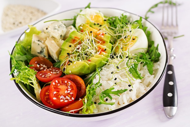 卵、米、トマト、アボカド、ブルーチーズとテーブルの上の健康的な緑のベジタリアンボウルランチ。