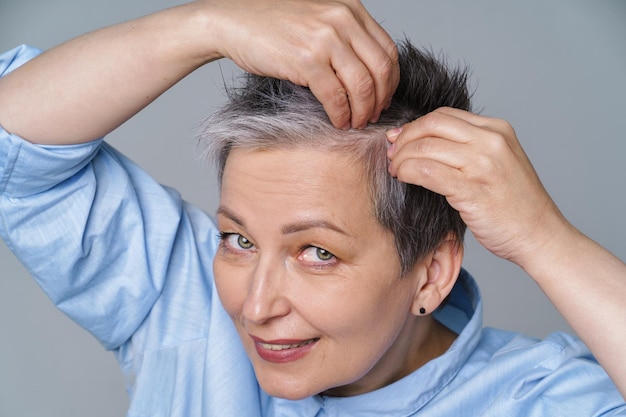 Healthy hair and lifestyle concept Beautiful grey haired woman dealing with dandruff problem checking in mirror