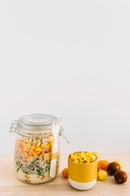 木製のテーブルにカップのメーソン瓶とコーンの種子の健康な自家製サラダ