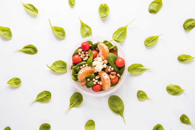 Healthy ingredients in bowl surrounded by leaves arranged on white backdrop