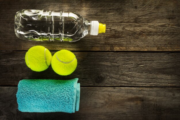 健康的なスポーツスポーツの概念。テニスボール、タオル、木の背景に水のボトル。スペースをコピーします。上面図。