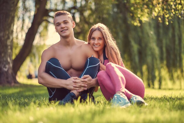 Healthy lifestyle concept. Happy young fitness couple cuddling while sitting on a green grass.