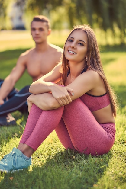 Healthy lifestyle concept. Happy young fitness couple cuddling while sitting on a green grass.