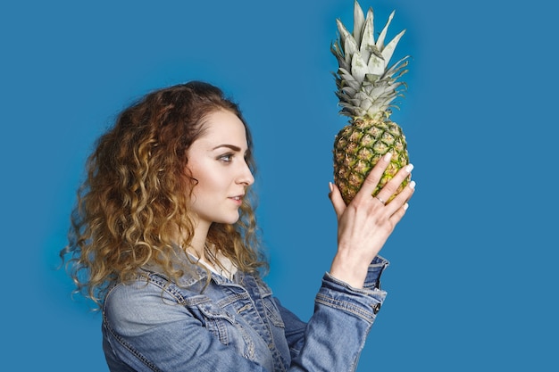 Stile di vita sano, fruttarismo, estate, dieta, cibo e concetto di nutrizione. ritratto laterale della giovane femmina caucasica alla moda con capelli ondulati che sceglie l'ananas dolce maturo per la macedonia