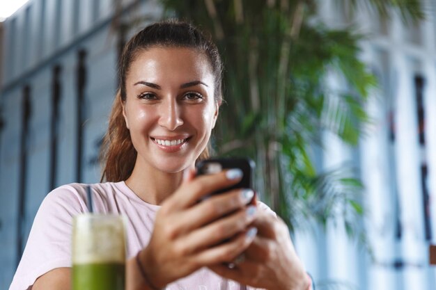 Healthy lifestyle people and leisure concept Closeup portrait of pretty caucasian female tourist woman using mobile phone while drinking smoothie on vacation travelling to beautiful island relax