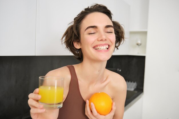 健康的なライフスタイルとスポーツ 美しい笑顔の女性 新鮮なオレンジジュースを飲み 果物を抱いて