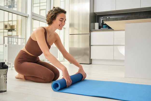 Free photo healthy lifestyle and sport fitness woman roll out her yoga matress for workout at home prepare wate