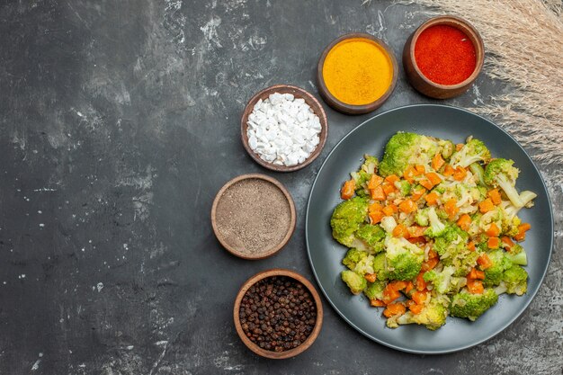 Здоровая еда с брокколи и морковью на черной тарелке и специями на сером столе