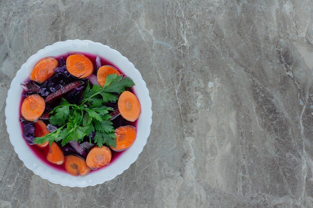 Healthy mix of beets, carrot slices and parsley garnish in a bowl on marble.