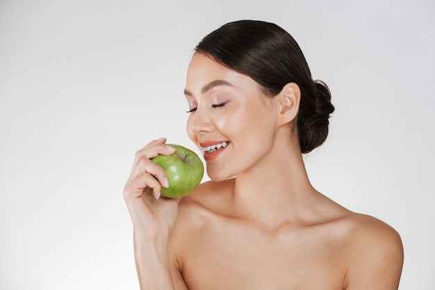 Здоровый портрет молодой женщины с мягкой свежей кожей, наслаждаясь зеленым сочным яблоком, изолированных на белый