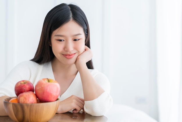 La felicità della donna abbastanza asiatica sana gode di mangiare e amare la dieta con la perdita di peso della frutta fresca della mela rossa il concetto di iedeas della stanza bianca dello sfondo interno