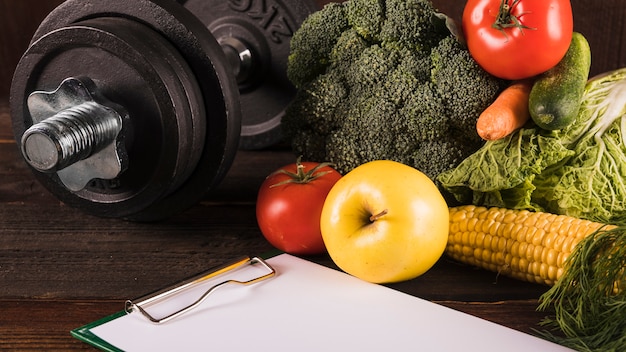 Healthy raw food and dumbbell on wooden surface