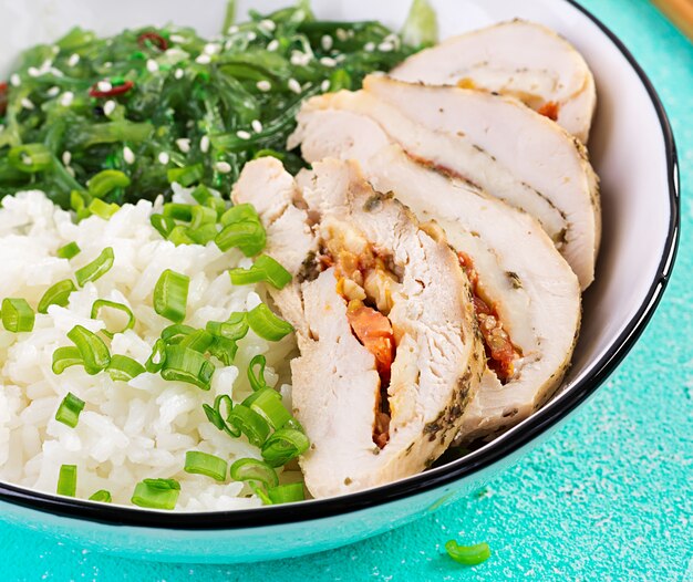 Healthy salad in a white bowl, chopsticks. Chicken rolls, rice, chuka and green onion. Blue table. Asian cuisine.