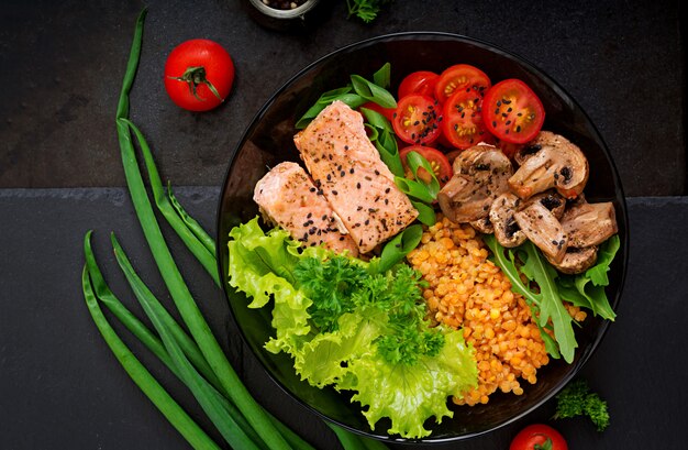 Полезный салат с лососем, помидорами, грибами, салатом и чечевицей на темном фоне