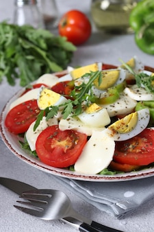 Healthy salad with tomatoes mozzarella olives arugula and eggs on a plate on a light background