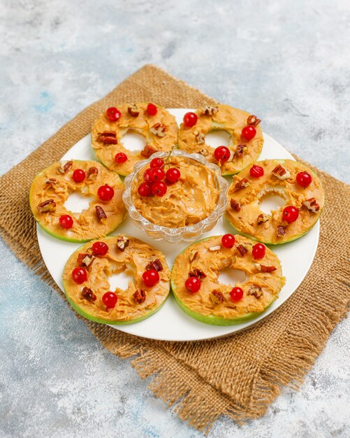 Free photo healthy sandwich. green apple rounds with peanut butter and red currant and pecan nuts on grey concrete, top view