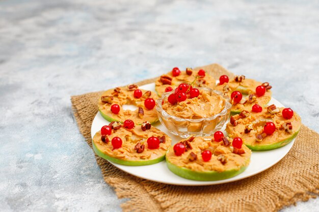 Free photo healthy sandwich. green apple rounds with peanut butter and red currant and pecan nuts on grey concrete, top view