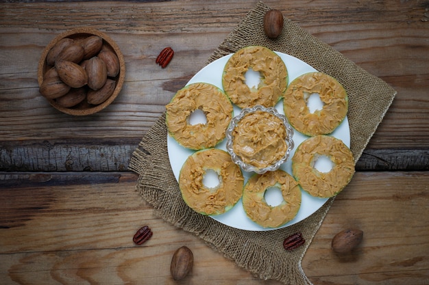 Healthy sandwich. Green apple rounds with peanut butter and red currant and pecan nuts on rustic, top view