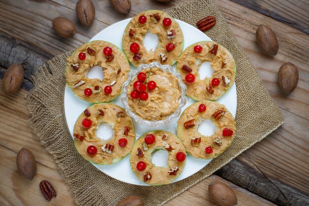 Healthy sandwich. Green apple rounds with peanut butter and red currant and pecan nuts on rustic, top view