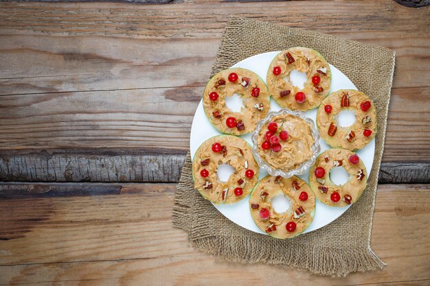 Healthy sandwich. Green apple rounds with peanut butter and red currant and pecan nuts on rustic, top view