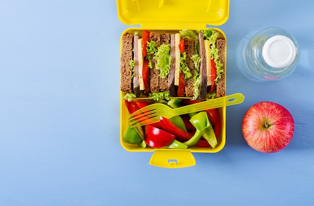 ビーフサンドイッチと新鮮な野菜、ボトル入りの水と青いテーブルに果物の健康的な学校のランチボックス。上面図。フラットレイ