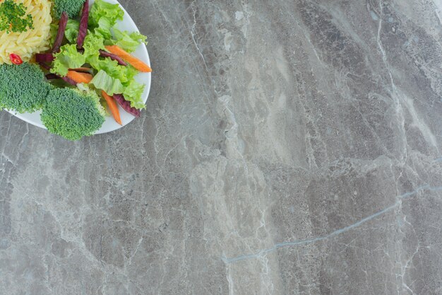 Healthy serving of pilau with chopped pepper, cabbage, greens, carrot and broccolie pieces on a platter on marble.