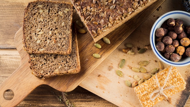 Здоровый хлеб из семян подсолнечника и миска из фундука с белковым баром на разделочной доске