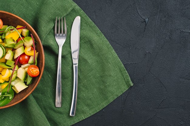 健康的な野菜のサラダフォークとバターナイフの黒い布を背景にテーブルクロスの上