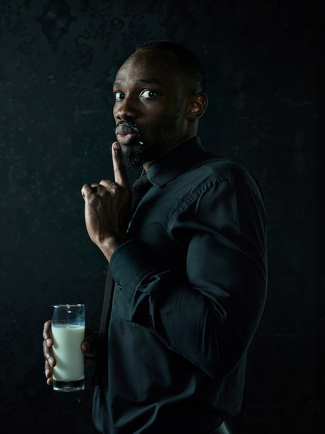 健康な若いアフリカ人男性がbllackスタジオで牛乳のカップを抱きしめています。
