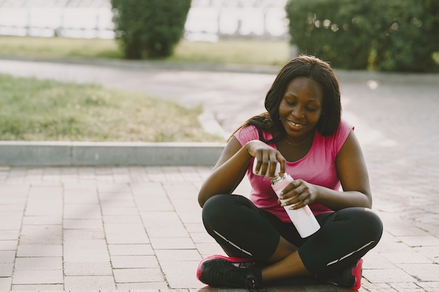 Healthy young african woman outdoors in morning. Girl with bottle of water.