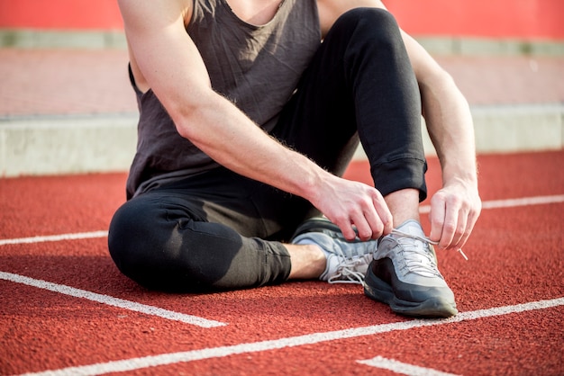 Free photo healthy young man sitting on running track tying his shoelace