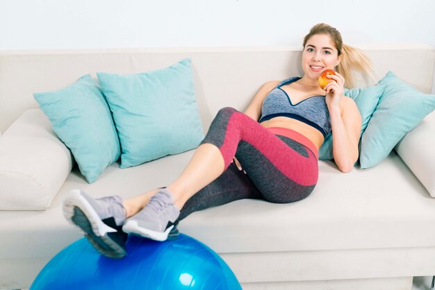 Healthy young woman holding apple in hand relaxing on sofa