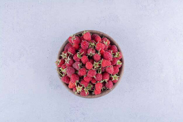 Heap of berries in a wooden bowl on marble background.