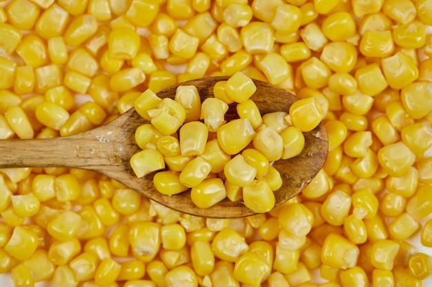 A heap of boiled sweet corn with a wooden spoon on a white table.