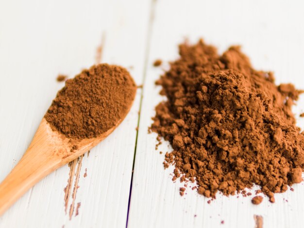 Heap of cocoa powder on table and in wooden spoon