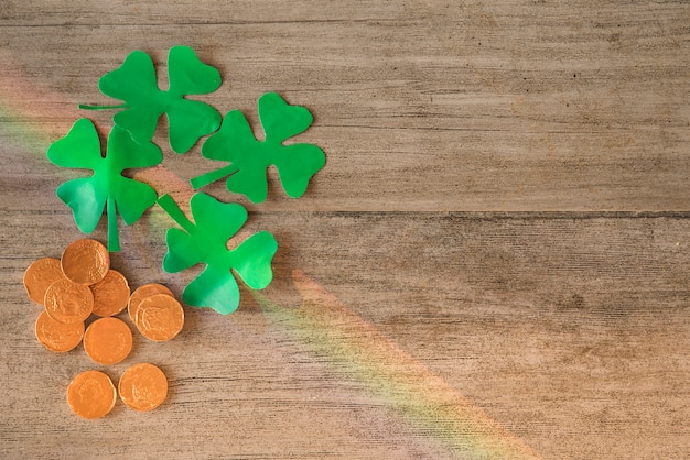 Heap of coins and green paper clovers on board