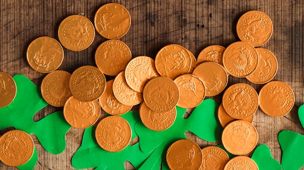 Free photo heap of coins and paper shamrocks on wooden table