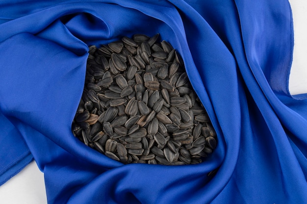 Heap full of sunflower black seeds placed on blue tablecloth 