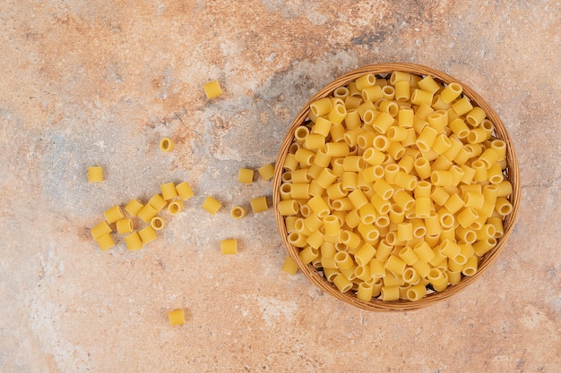 Heap of raw Ditalini pasta on wooden basket