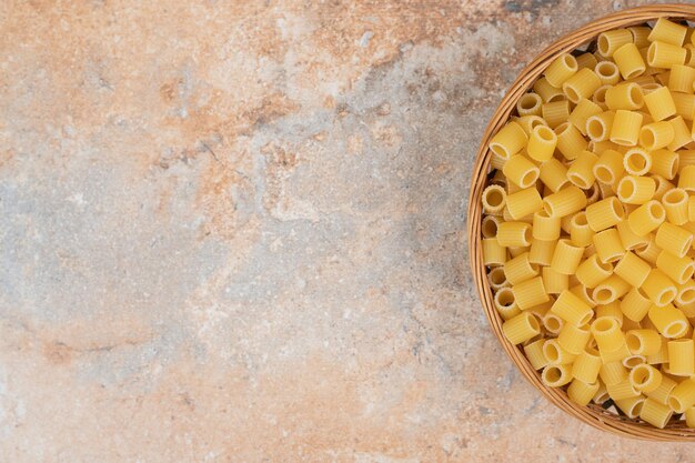 Heap of raw Ditalini pasta on wooden basket. 